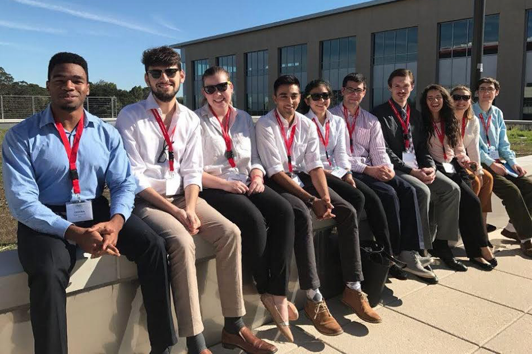 10 students who attended PhysCon 2016 sit in a line, smiling and wearing red lanyards with badges