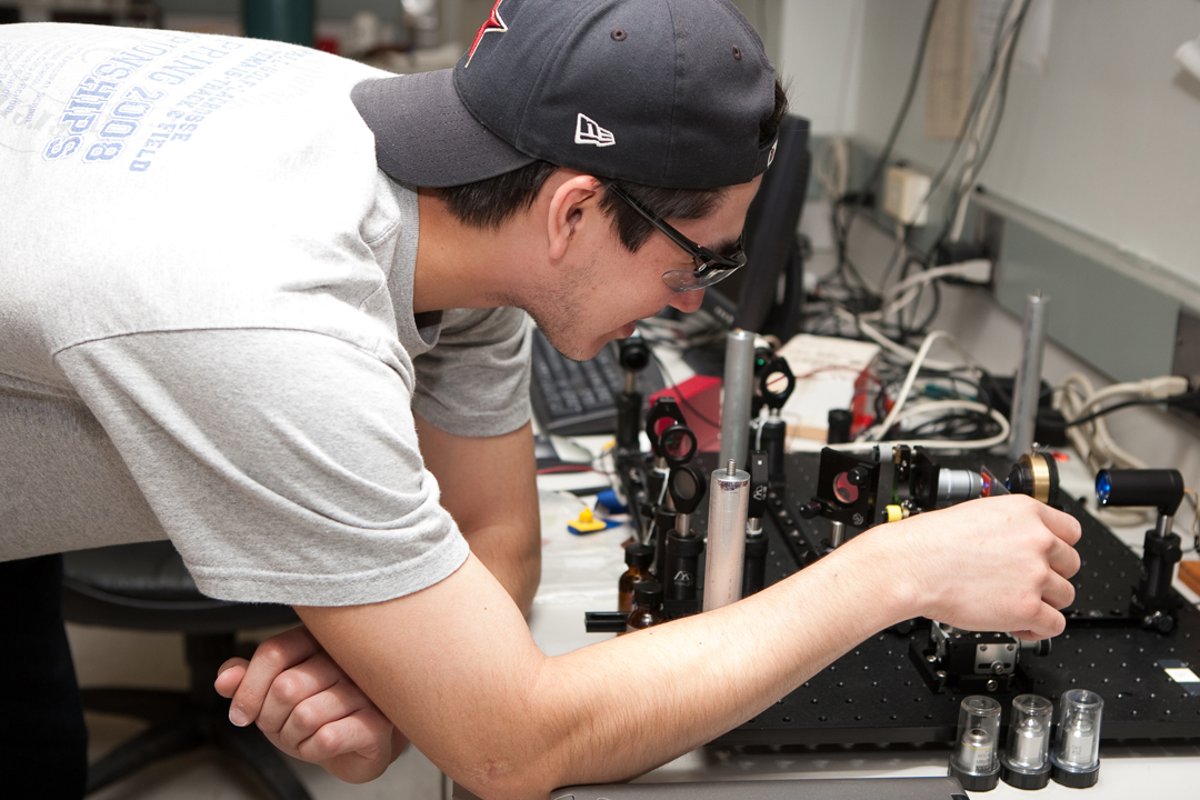 A male physics student touching an optical device on a desk