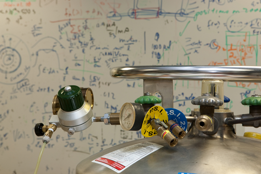 A nitrogen tank with a white board covered in formulas in the background