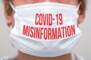 The lower half of a man's face is photographed here. He is wearing a medical face mask that reads, "COVID-19 Misinformation" in all red text