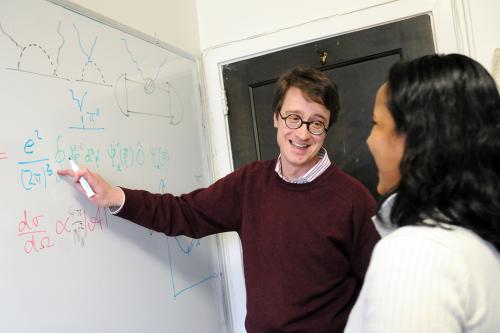 Professor of Physics Harald Griesshammer (left) point at a white board while talking to a female student (right)