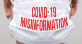 The lower half of a man's face is photographed here. He is wearing a medical face mask that reads, "COVID-19 Misinformation" in all red text